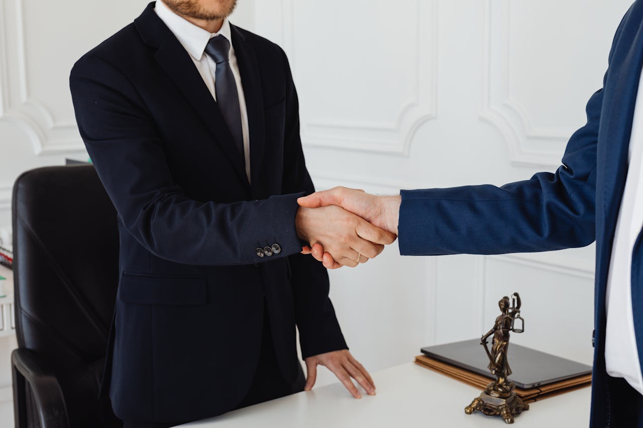 About Two men in suits shaking hands in a formal office environment symbolizing an agreement.